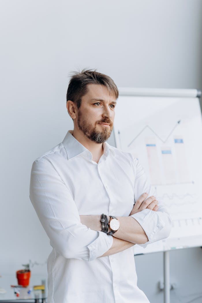Professional bearded man with arms crossed in a modern office space, looking focused.